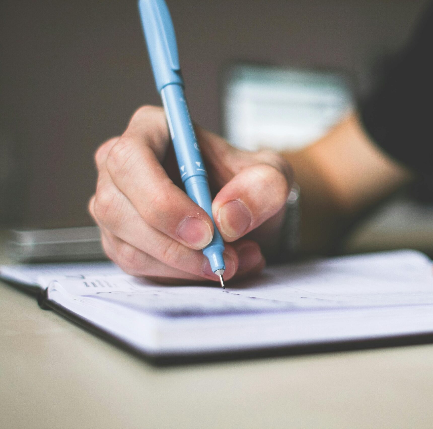 Close-up of hand writing in notebook using a blue pen, focus on creativity.